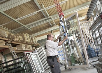 Ein fertig montiertes Fenster wird mittels Kran vom Arbeitstisch angehoben und zum Transportwagen gebracht