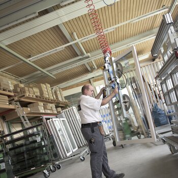 Ein fertig montiertes Fenster wird mittels Kran vom Arbeitstisch angehoben und zum Transportwagen gebracht